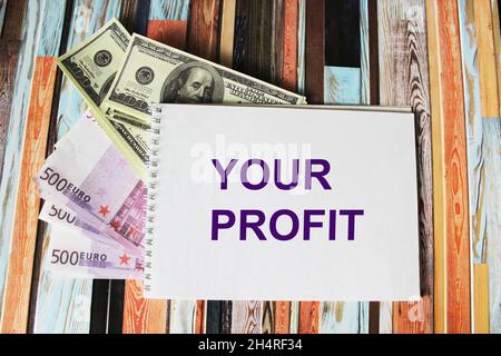 Notizblock mit dem Text IHR GEWINN, Ihre Dollars und Euros liegen auf einem farbig gestreiften Hintergrund. Stockfoto