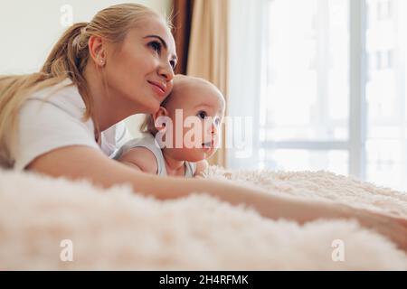 Frau, die mit ihrem Baby auf dem Bett liegt. Mutter umarmt Kind. Familie entspannt zu Hause verbringen Zeit zusammen Stockfoto