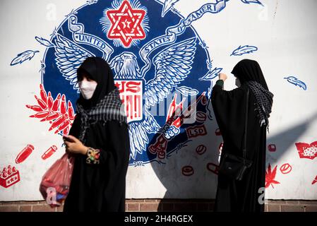 Teheran, Iran. November 2021. Zwei Frauen gehen bei einer Kundgebung vor der ehemaligen US-Botschaft am Donnerstag, den 4. November 2021, an einem Anti-US-Graffiti vorbei, um an dem Jahrestag ihrer Festnahme im Jahr 1979 in Teheran, Iran, zu erinnern. Die Übernahme der Botschaft löste eine 444-tägige Geiselkrise und einen Bruch der diplomatischen Beziehungen aus, die bis heute andauert. (Foto: Sobhan Farajvan/Pacific Press/Sipa USA) Quelle: SIPA USA/Alamy Live News Stockfoto