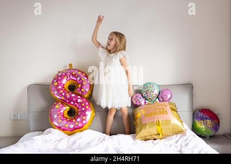 Indoor-Aufnahme von ziemlich fröhlich niedlichen entzückenden Mädchen Kind feiert acht Jahre alten Geburtstag mit hellen und bunten Ballons mit Inschrift Worte bleiben Stockfoto