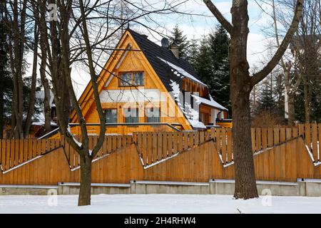 Zakopane, Polen - 21. März 2018: Das hinter dem Holzzaun verborgene Holzgebäude ist mit einem steilen Dach bedeckt. Um sie herum gibt es einige Bäume Stockfoto