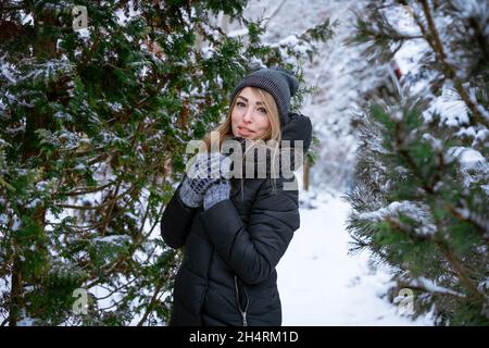 Schöne lächelnde junge Frau im Winter im Freien in warmer Jacke genießt Wetter unter den schneebedeckten Bäumen. Kaukasisches Mädchen auf einem Spaziergang im Winter. Winterkonzept Stockfoto