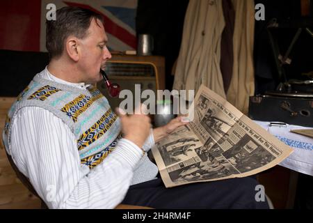 Großbritannien der 1940er Jahre: Mann raucht Pfeife, liest Zeitung, während er auf Schallplatte zugehört. Stockfoto