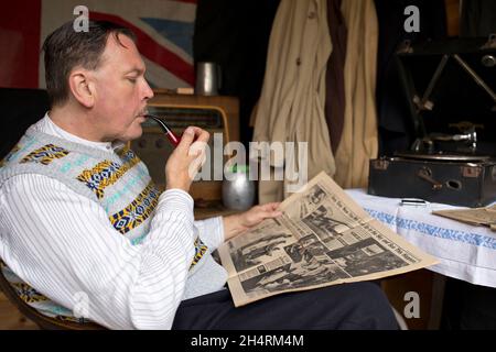 Großbritannien der 1940er Jahre: Mann raucht Pfeife, liest Zeitung, während er auf Schallplatte zugehört. Stockfoto