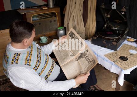 Großbritannien der 1940er Jahre: Mann raucht Pfeife, liest Zeitung, während er auf Schallplatte zugehört. Stockfoto