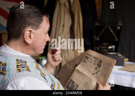 Großbritannien der 1940er Jahre: Mann raucht Pfeife, liest Zeitung, während er auf Schallplatte zugehört. Stockfoto