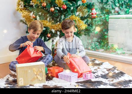 Zwei Kinder am Weihnachtsbaum öffnen ihre Geschenke vom Weihnachtsmann oder den drei Weisen und teilen ihre Spielsachen Stockfoto