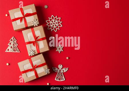 Weihnachtsgeschenke Kraftboxen mit rotem Band und umweltfreundlichem Weihnachtsbaumspielzeug aus Holz auf rotem Hintergrund. Das Konzept von Weihnachten, Neujahr backgr Stockfoto