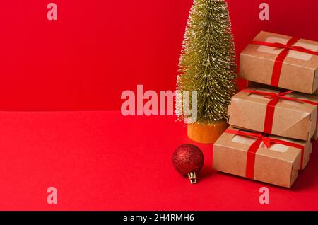 Ein Haufen Weihnachtsgeschenke aus Kraftkarton mit rotem Band, Öko Baum auf rotem Hintergrund. Das Konzept des Feiertags des Tages der Geschenke Stockfoto