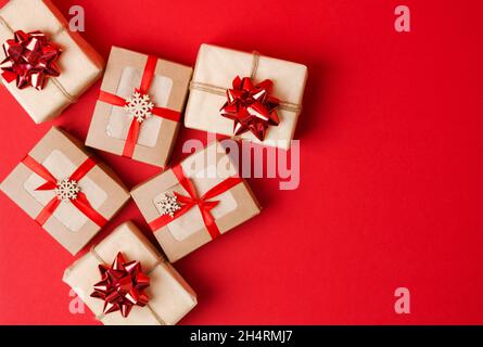 Weihnachten, Neujahr. Geschenke in Kraftpapier und Kraftboxen mit rotem Band und Schleifen auf rotem Hintergrund Stockfoto