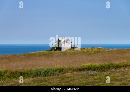 Weiß verlassene, baufällige Bauernhaus mit einigen Ackerland an der Nordküste von Island mit Panoramablick auf den Ozean gegen einen blauen Himmel in der Stockfoto