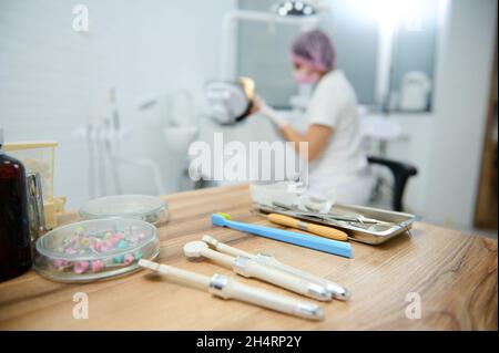 Moderne Dentalwerkzeuge, sterile Edelstahlinstrumente auf einer Holzoberfläche vor einem verschwommenen Hintergrund eines Zahnarztes, der Karies an einen Patienten in behandelt Stockfoto