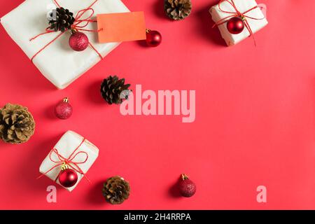 Die Neujahrsgeschenke sind in Bastelpapier gewickelt und mit einem roten Gummis gebunden, liegen zwischen den Kugeln und Zapfen auf einem roten Hintergrund. Handgefertigte Verpackung. Draufsicht. Stockfoto