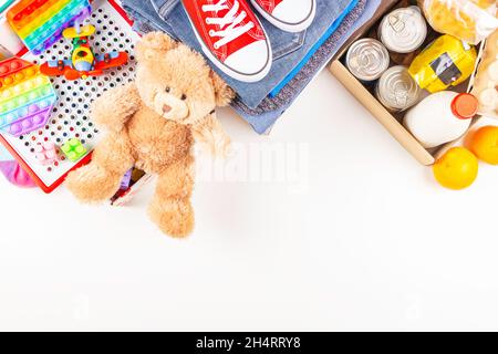 Spende, Wohltätigkeitskonzept. Lebensmittel-Spendenboxen mit Lebensmittelprodukten, Kleidung und Kinderspielzeug auf weißem Tisch. Draufsicht, Kopierbereich Stockfoto