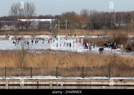 OEGSTGEEST, NIEDERLANDE - 15. Feb 2021: Eine große Anzahl von Menschen, die auf einem gefrorenen Feuchtgebiet in der Nähe eines Wohngebiets im Westen der Niederlande sabotieren Stockfoto