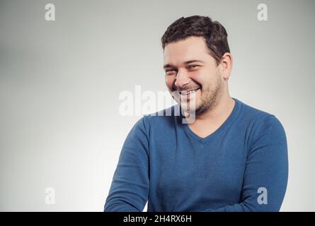 Junge lachende Mann Porträt in blauen Pullover im Studio-Hintergrund Stockfoto