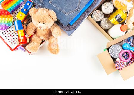 Spende, Wohltätigkeitskonzept. Lebensmittel-Spendenboxen mit Lebensmittelprodukten, Kleidung und Kinderspielzeug, Tiernahrung und Vorräten für Unterstände auf weißem Tisch. Oben Stockfoto