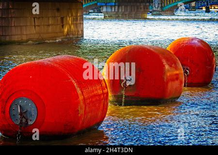 Boys, Ahoi! - Eine Linie von drei schwimmenden orangefarbenen Bojen auf der Themse in der Londoner Innenstadt. Stockfoto