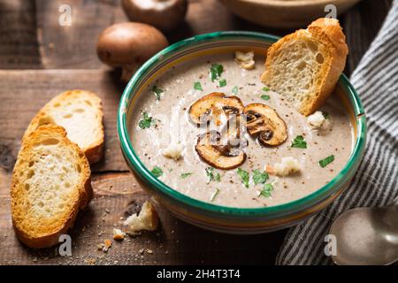 Hausgemachte cremige Pilzsuppe mit aufgeschnittenen Pilzen in einer alten Schüssel und Brot Toast auf einem rustikalen Holztisch Stockfoto