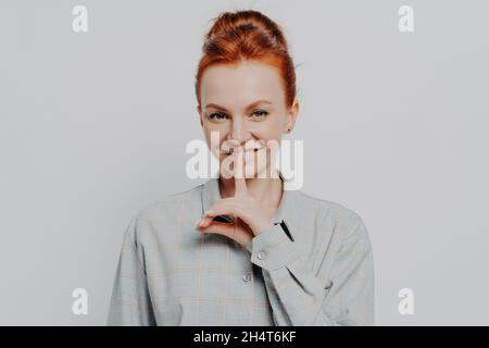 Fröhliche junge Ingwer 30er Jahre Frau zeigt Stille Geste, während posiert isoliert auf grauen Studio-Hintergrund Stockfoto
