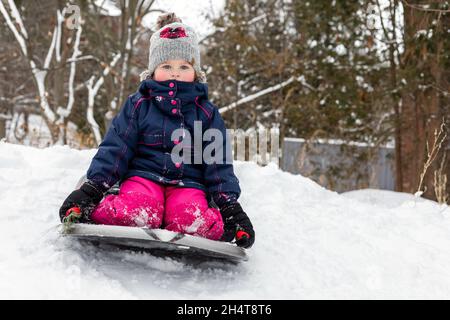 Kind, das im Winter bei schneebedecktem kaltem Wetter im Schlitten im Freien sitzt. Mädchen mit Rodel. Stockfoto