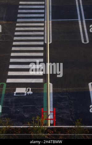 Parkplatz mit roter Schutzstruktur für Strommast, seitlich ist der Bereich sichtbar, der für das Laden von Elektroautos und Fußgängerüberweg reserviert ist. Stockfoto