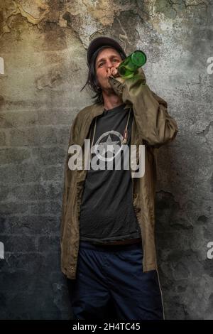 Junkie Mann mit Mütze grün Anorak und blaue Jogginghose in der Nähe Stein alten Wand Stockfoto