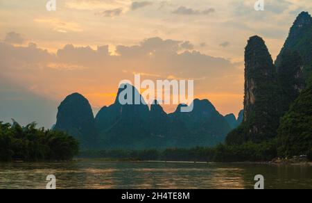 Die Kalksteinkarsthügel entlang des Flusses Li in der Nähe von Xingping, China, mit kleinen Touristenflößen auf dem Fluss. Stockfoto