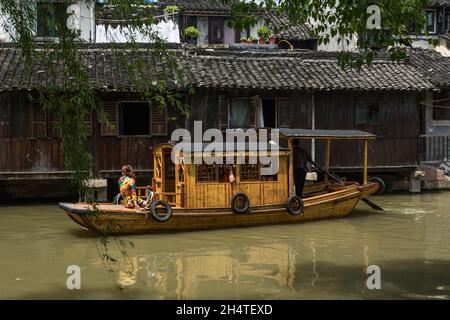 Touristen in einem traditionellen Holzboot auf dem Kanal in Dong Zhu oder Ost-Wuzhen, der Wasserstadt Chinas. Stockfoto