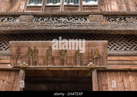 Aufwendige Holzschnitzereien und ein Zeichen in chinesischer Kalligraphie auf der Vorderseite eines alten Gebäudes in Wuzhen, China. Stockfoto