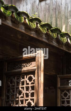 Aufwendige Entwürfe auf verdeckten Tonfliesen über einem hölzernen Gitterfenster eines alten Gebäudes in Wuzhen, China. Stockfoto