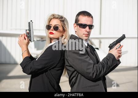Professionelle Bodyguards für weibliche und männliche Spionageagenten, die mit Gewehren posieren. Sicherheitspolizei-Team in zivilem schwarzen Anzug mit Sonnenbrille Stockfoto
