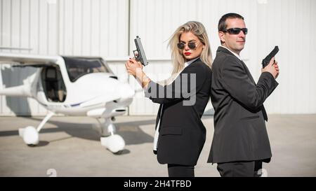 Professionelle Bodyguards für weibliche und männliche Spionageagenten, die mit Gewehren posieren. Sicherheitspolizei-Team in zivilem schwarzen Anzug mit Sonnenbrille Stockfoto