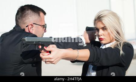 Professionelle Bodyguards für weibliche und männliche Spionageagenten, die mit Gewehren posieren. Sicherheitspolizei-Team in zivilem schwarzen Anzug mit Sonnenbrille Stockfoto