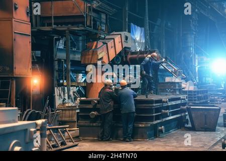 Innen des Stahlwerks. Die Arbeiter in der Werkstatt der metallurgischen Anlage. Gebäude der Gießerei und der Schwerindustrie im Hintergrund.