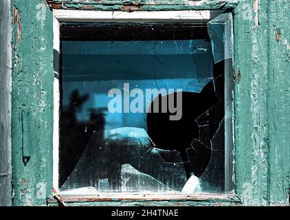 Kaputtes Fenster. Gebrochenes Glas mit Loch. Vandalismus, Zerstörung und Unfallkonzept. Stockfoto