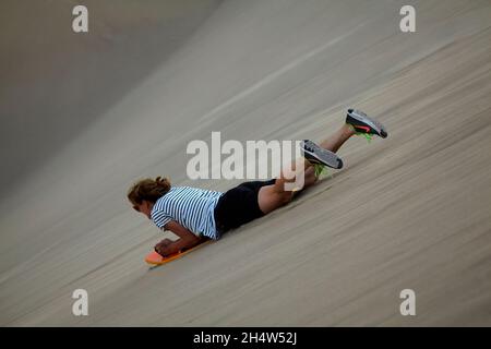 Sandboarding von Frauen auf Dünen in der Nähe der Oase Huacachina, in der Nähe von Ica, Peru, Südamerika (MR) Stockfoto