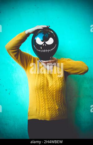 Mädchen im Hof hält aufblasbaren Ballon mit einem bösen Gesicht in ihren Händen außerhalb Happy halloween Konzept Holiday Card Street Style Herbst Saison Kostüm Stockfoto
