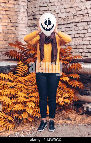 Mädchen im Hof hält aufblasbaren Ballon mit einem bösen Gesicht in ihren Händen außerhalb Happy halloween Konzept Holiday Card Street Style Herbst Saison Kostüm Stockfoto