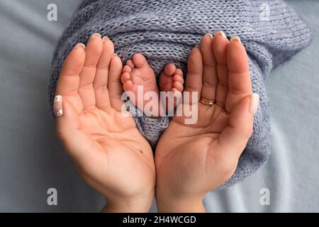 Beine, Zehen, Füße und Fersen eines Neugeborenen. Mit den Händen der Eltern, Vater, Mutter hält sanft die Beine des Kindes. Stockfoto