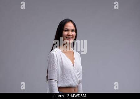 Attraktive Frau mit freundlichem Lächeln und langen dunklen Haaren, die ein stilvolles weißes Spitzen-Top in einem Oberkörperportrait trägt Stockfoto