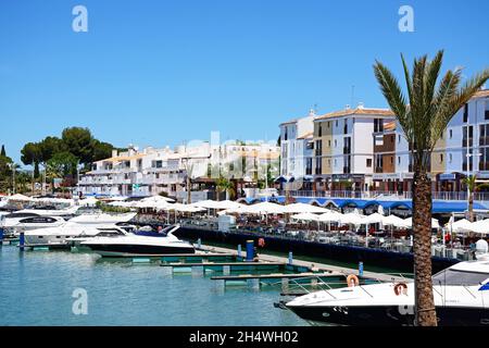 Luxusboote, die in der Marina mit Restaurants am Wasser auf der Rückseite, Vilamoura, Algarve, Portugal, Europa, festgemacht sind. Stockfoto