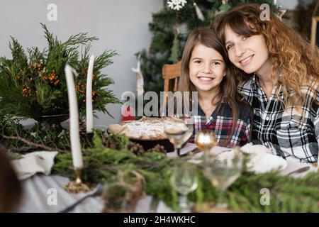 Familie zu Weihnachten am Festtisch. Portrait einer glücklichen Mutter und Tochter an einem dekorierten Tisch im Wohnzimmer. Kerzen, Zweige Stockfoto