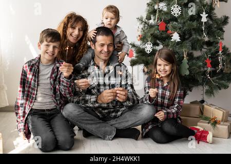 Glückliche volle Familie und drei Kinder zu Hause mit Weihnachtsgeschenken sitzen zu Hause am Morgen unter einem Weihnachtsbaum im Winter auf dem Boden. Stockfoto