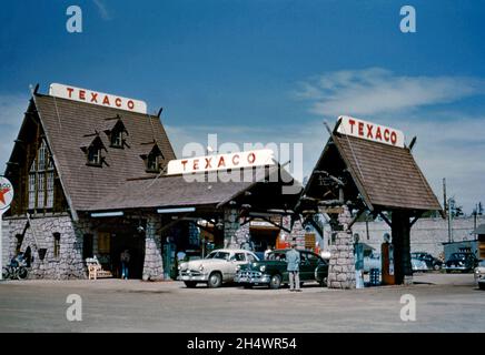 Die ungewöhnliche und unverwechselbare Stein- und Holzarchitektur der Texaco-Tankstelle von Walt Stuart an der Ecke Canyon Street und Yellowstone Avenue, West Yellowstone, Montana, USA c. 1954. Autos werden mit Gas gefüllt. Dieses Bild stammt aus einer alten amerikanischen Kodak Amateur-Farbtransparenz – einem Vintage-Foto aus den 1950er Jahren. Stockfoto