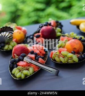Fruchtmischung. Pfirsich, Trauben, Apfel, Wassermelone, Melone. Obststücke auf einem Teller auf dunklem Grund. Natürliches Lebensmittelkonzept Stockfoto