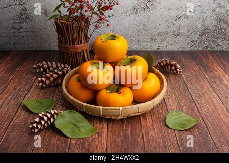 Süße Kaki im Bambuskorb. Vorderansicht, Holztisch Hintergrund und Zentrum Persimmon Set. Stockfoto