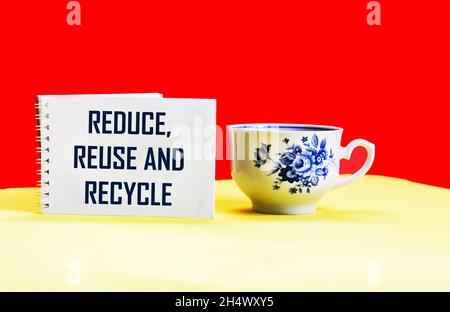 Text Reduzieren, wiederverwenden und recyceln auf Notizblock und rotem und gelbem Hintergrund mit schöner Tasse Stockfoto