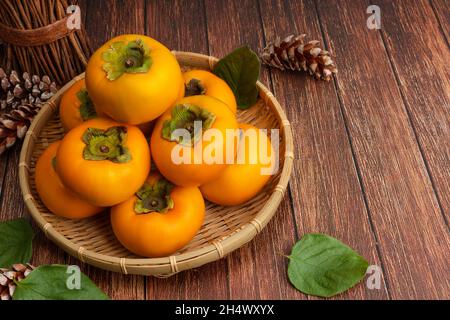 Süße Kaki im Bambuskorb. Draufsicht, Holztisch Hintergrund und Kaki Set. Stockfoto