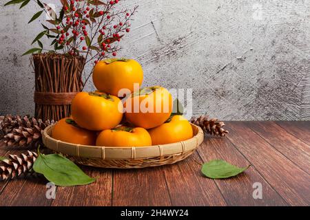 Süße Kaki im Bambuskorb. Holztisch Hintergrund mit einem Satz von Kaki auf der linken Seite. Stockfoto